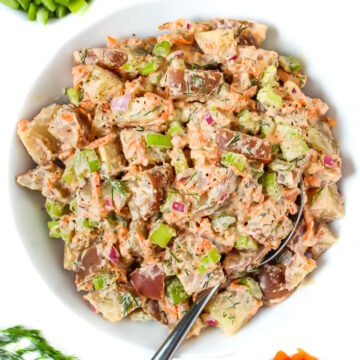 Vegan potato salad with creamy dressing in a white bowl with serving spoon