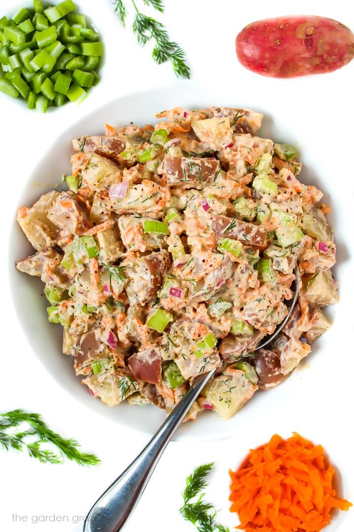 Vegan potato salad with creamy dressing in a white bowl with serving spoon