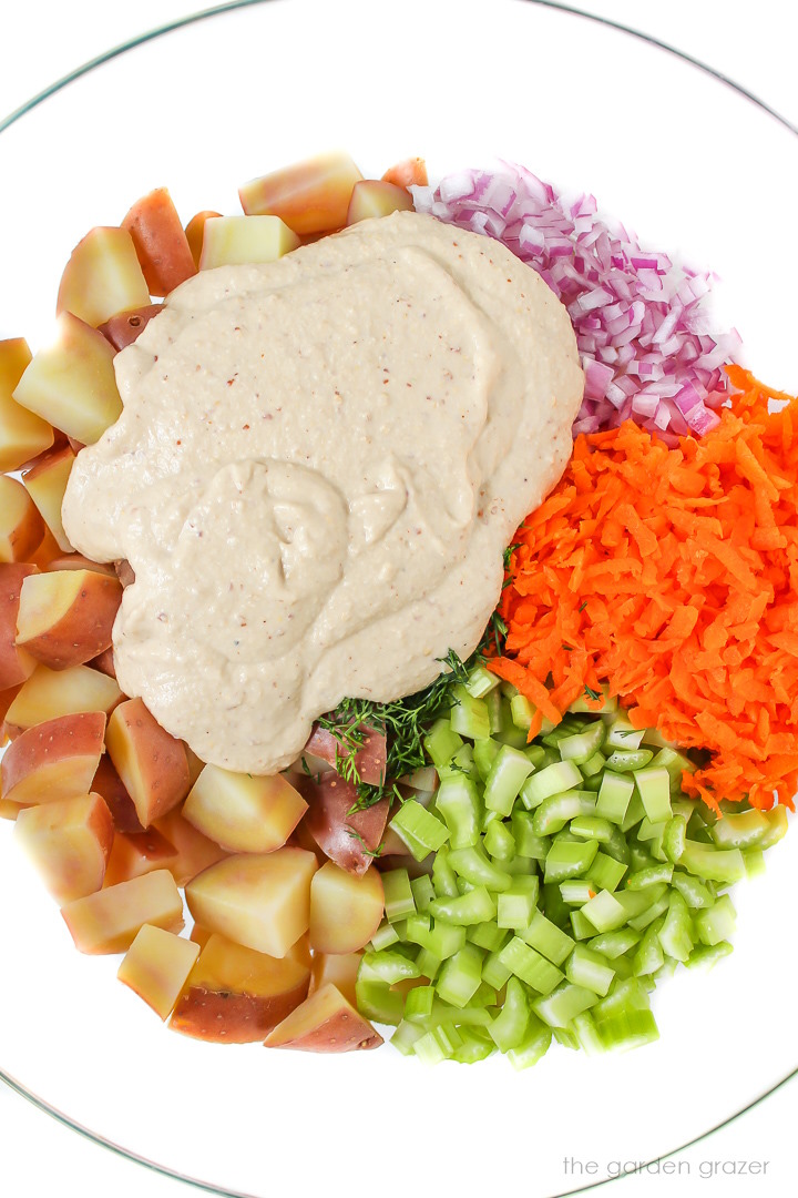 Vegan potato salad ingredients in a bowl before mixing with creamy dressing on top