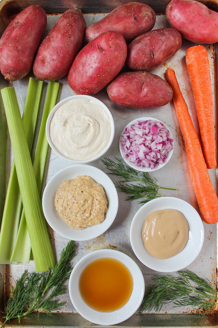 Red fingerling potatoes, celery, carrots, onion, mayo, and fresh dill ingredients laid out on a metal tray