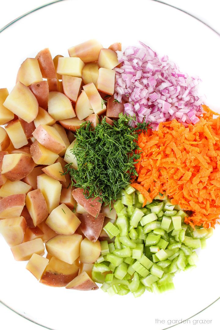 Cooked potatoes and prepared veggies in a glass bowl before mixing