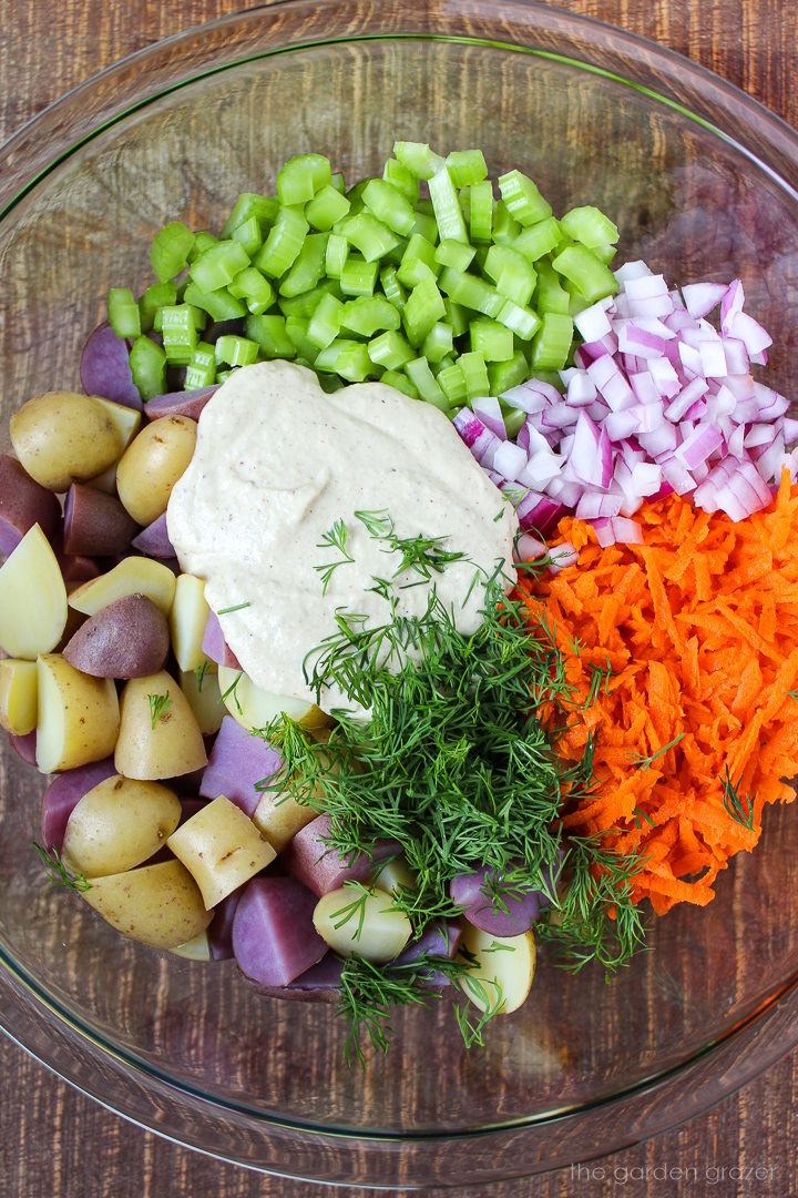 Preparing chopped veggies in a large glass bowl topped with a homemade mayo mustard dressing