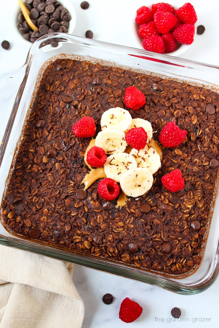 Brownie baked oatmeal in a glass baking dish topped with banana, raspberries, and peanut butter