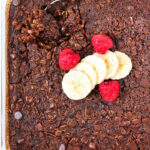 Vegan brownie baked oatmeal in a glass baking dish topped with banana and raspberries