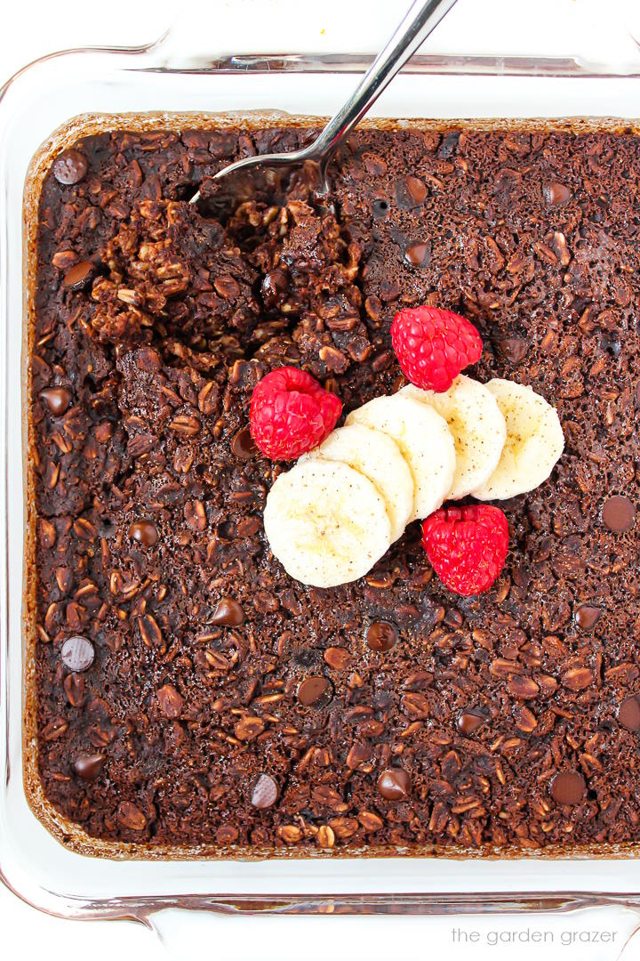 Vegan brownie baked oatmeal in a glass baking dish topped with banana and raspberries
