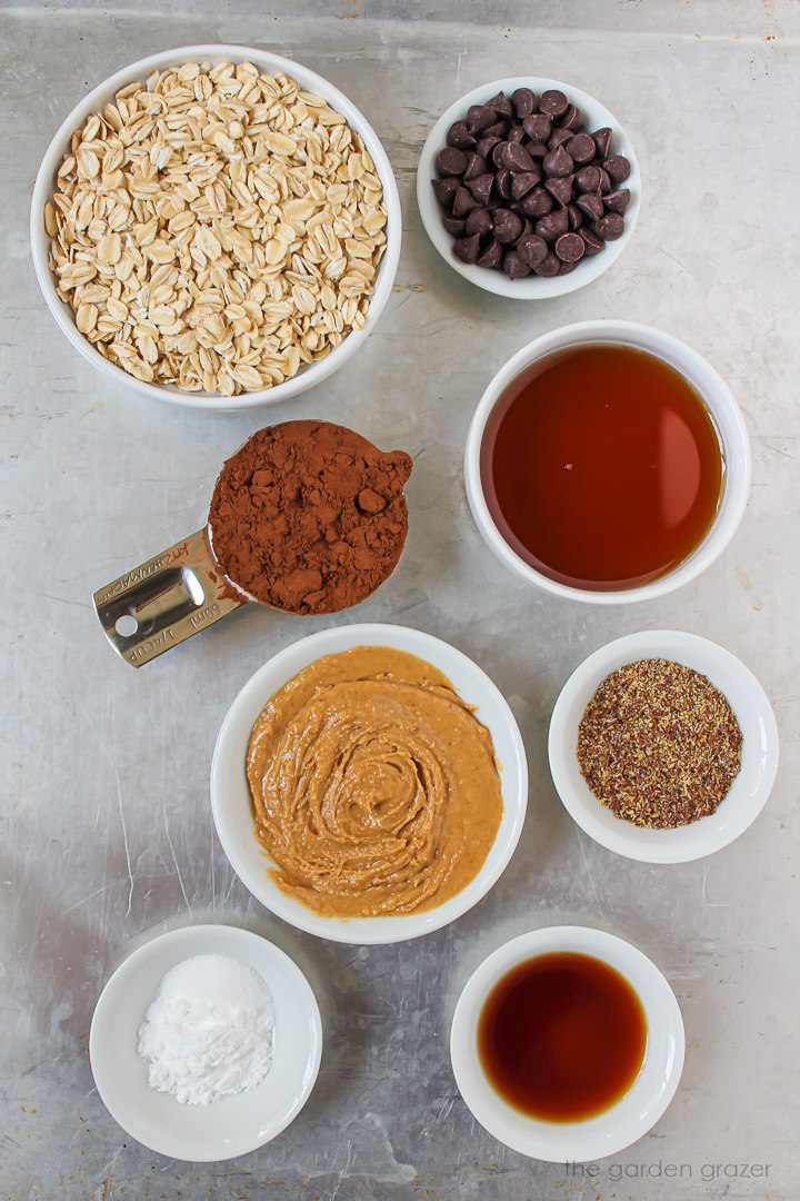 Oats, cocoa powder, peanut butter, flax, maple syrup, and vanilla ingredients laid out on a metal tray