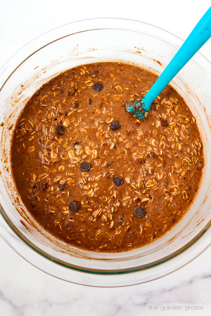 Brownie baked oatmeal batter mixed together in a glass bowl with spatula