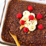 Vegan brownie baked oatmeal in a glass baking dish with serving spoon
