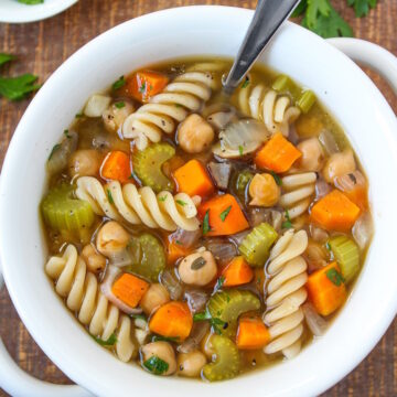 Chickpea noodle soup in a white bowl with serving spoon sitting on a wooden table