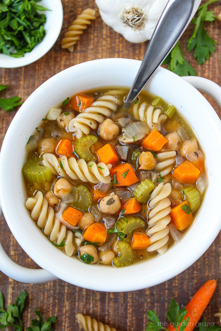 Chickpea noodle soup in a white bowl with serving spoon sitting on a wooden table