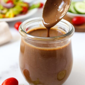A spoon lifting up creamy balsamic dressing from a small glass jar