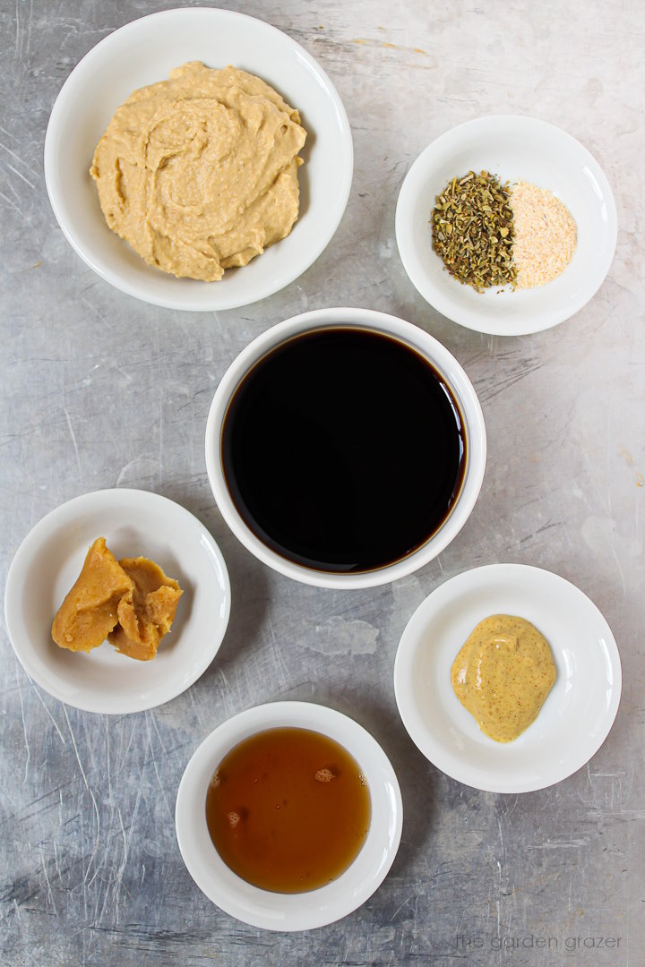 Vinegar, mustard, hummus, miso, and spice ingredients laid out in white bowls on a metal tray