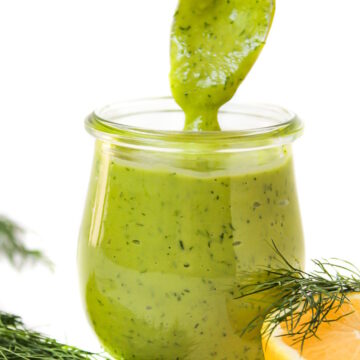 Serving spoon scooping out creamy dill dressing from a small glass jar