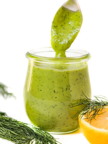 Serving spoon scooping out creamy dill dressing from a small glass jar