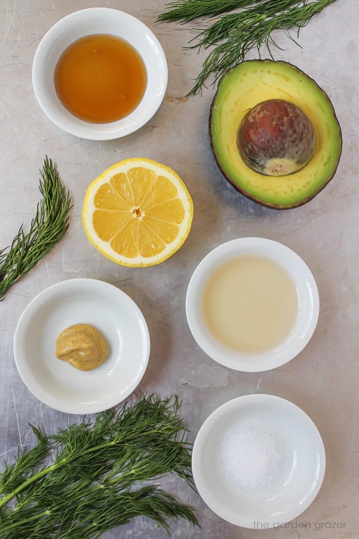 Lemon, avocado, fresh herbs, mustard, and vinegar ingredients laid out on a metal tray