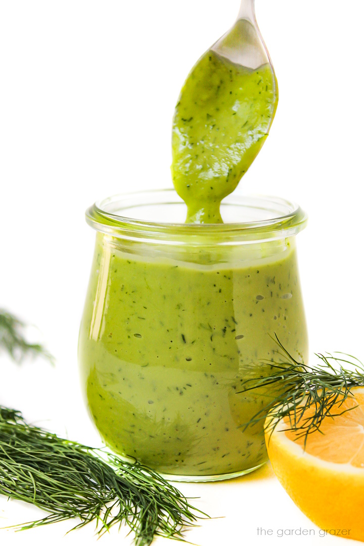 Serving spoon scooping out creamy dill dressing from a small glass jar