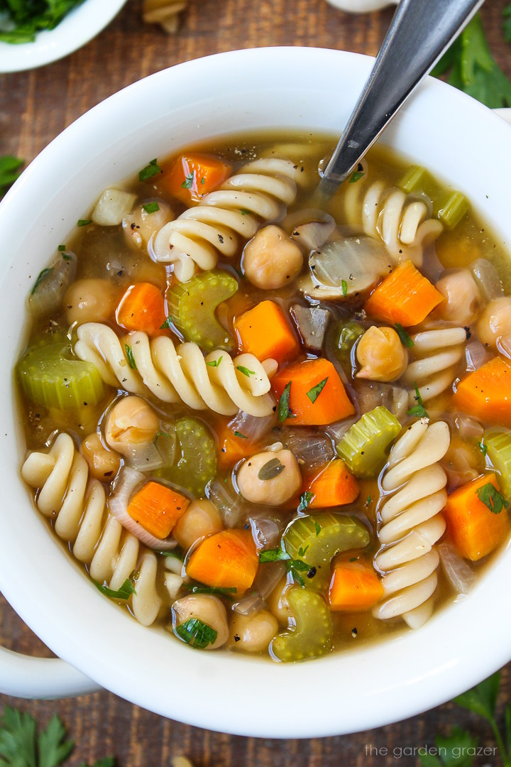 Close-up view of chickpea noodle soup in a white bowl with serving spoon