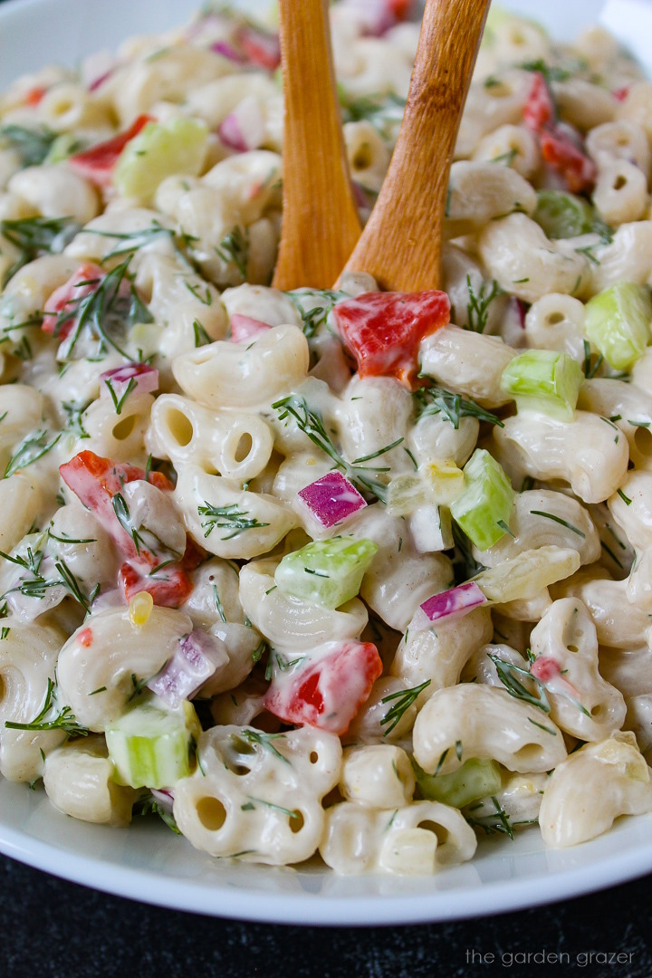 Close up view of vegan macaroni salad in a white bowl with wooden serving spoons