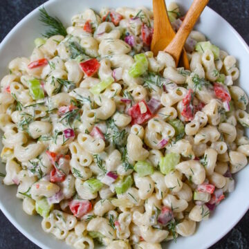 Vegan macaroni salad with creamy dressing in a white serving bowl with wooden spoons