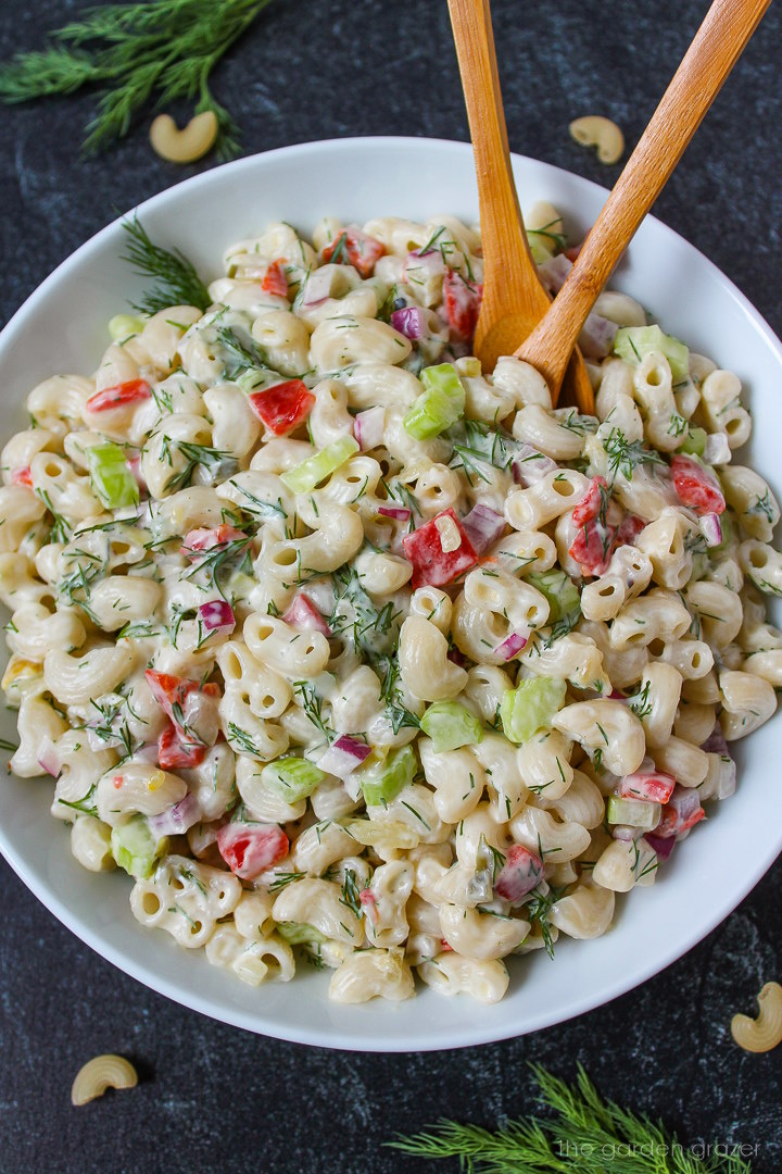 Vegan macaroni salad with creamy dressing in a white serving bowl with wooden spoons