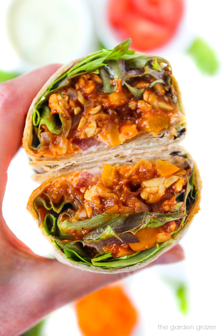 Hand holding a BBQ ranch tempeh wrap cut in half to show inside