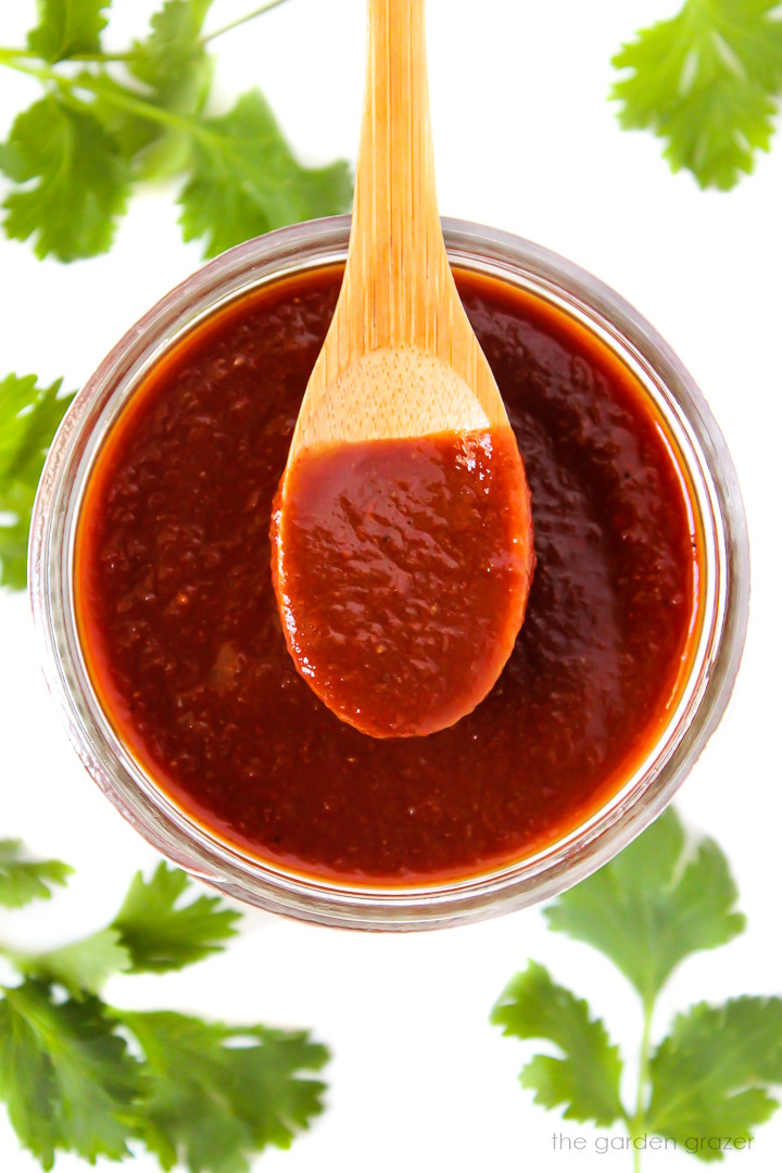 Overhead view of vegan BBQ sauce in a glass jar with wooden spoon