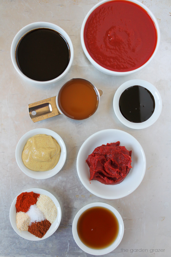 Tomato sauce, molasses, mustard, vinegar, tomato paste, and spice ingredients laid out on a metal tray