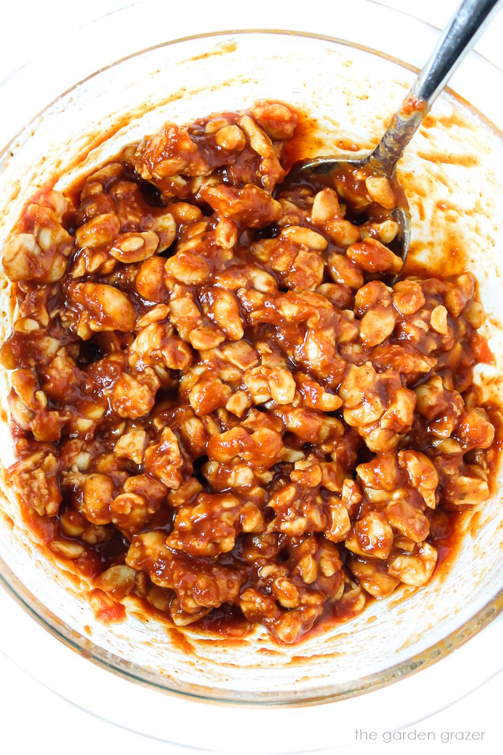 Overhead view of crumbled tempeh marinating in BBQ sauce with metal spoon
