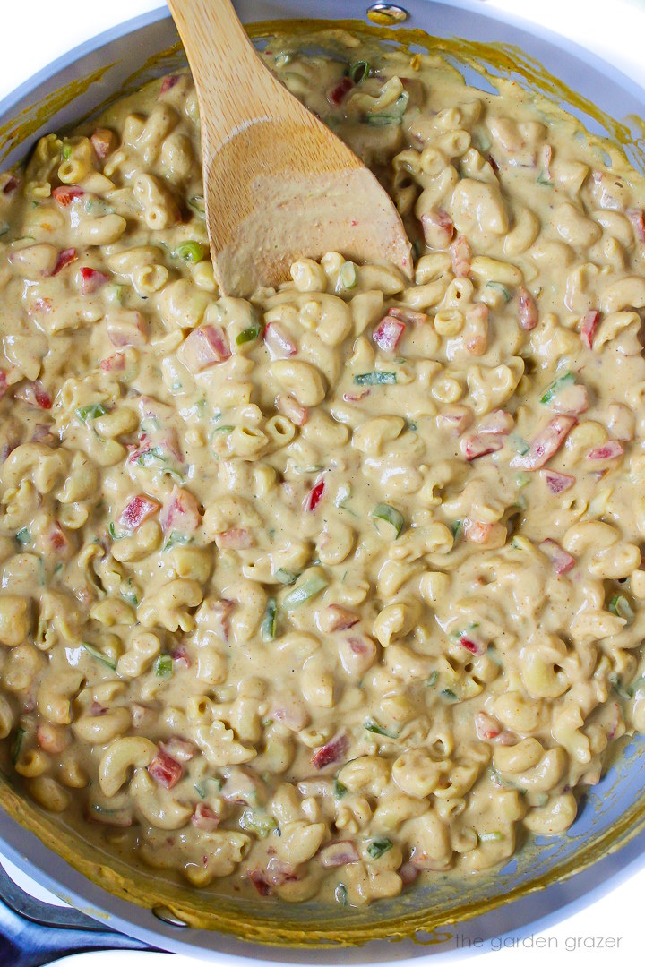 Vegan Mexican mac and cheese cooking in a large skillet with stirring spoon