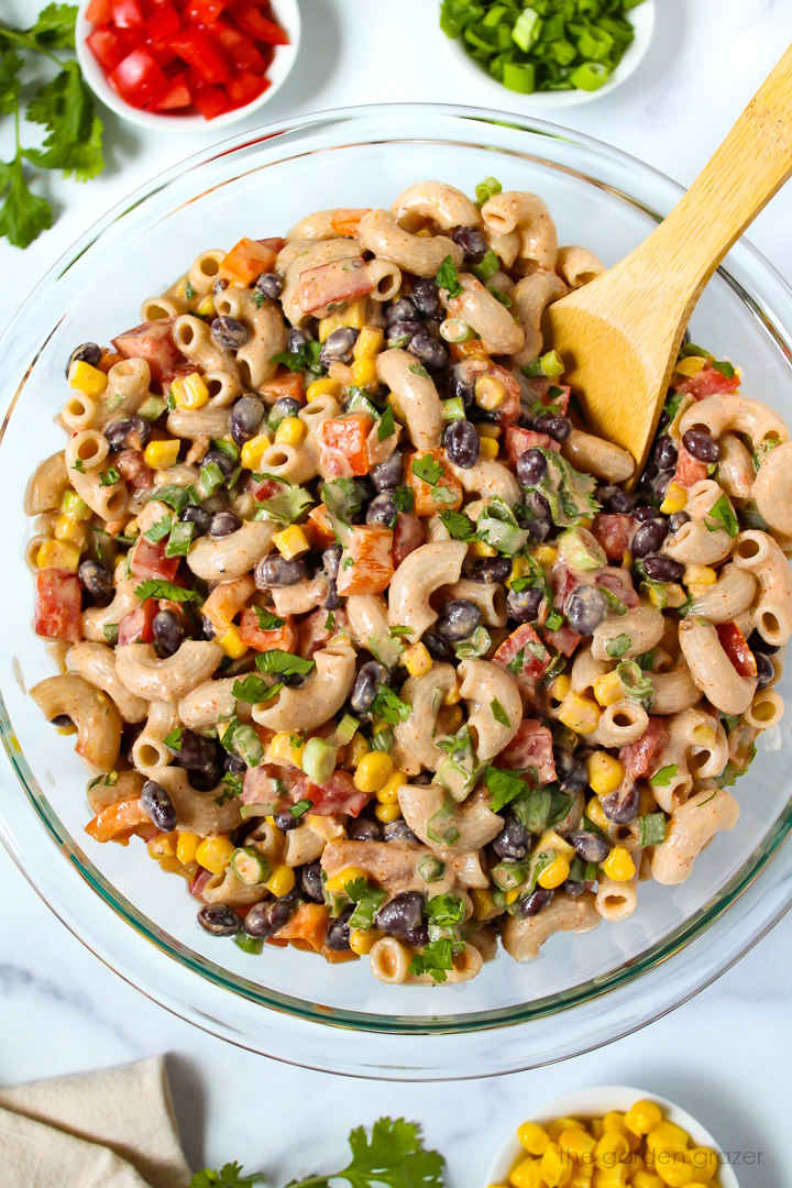 Preparing Mexican macaroni salad in a large mixing bowl with wooden spoon