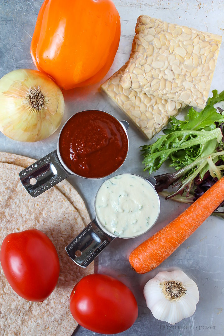 Bell pepper, onion, tomato, tortillas, garlic, carrot, and greens ingredients laid out on a metal tray