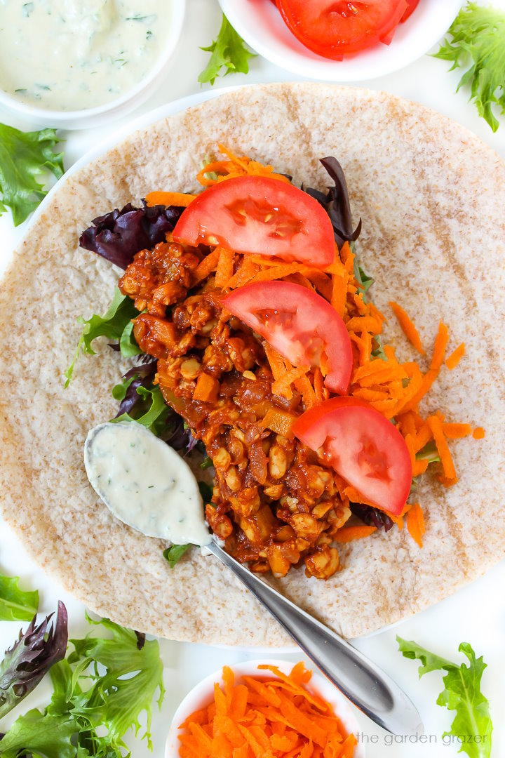 Preparing an open-faced wrap with BBQ tempeh, greens, tomato, and ranch dressing