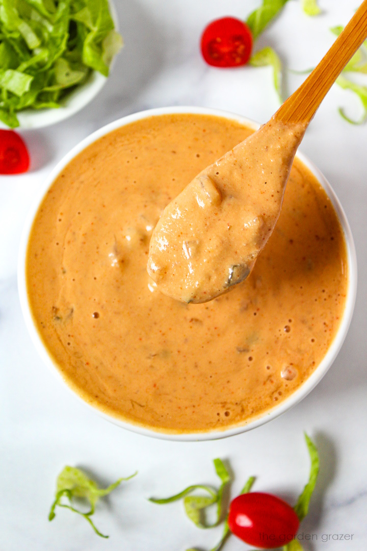 Overhead view of preparing vegan thousand island dressing in a white bowl with wooden serving spoon