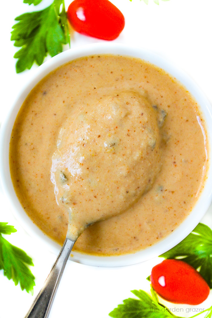 Spoon scooping out vegan thousand island dressing from a small white bowl
