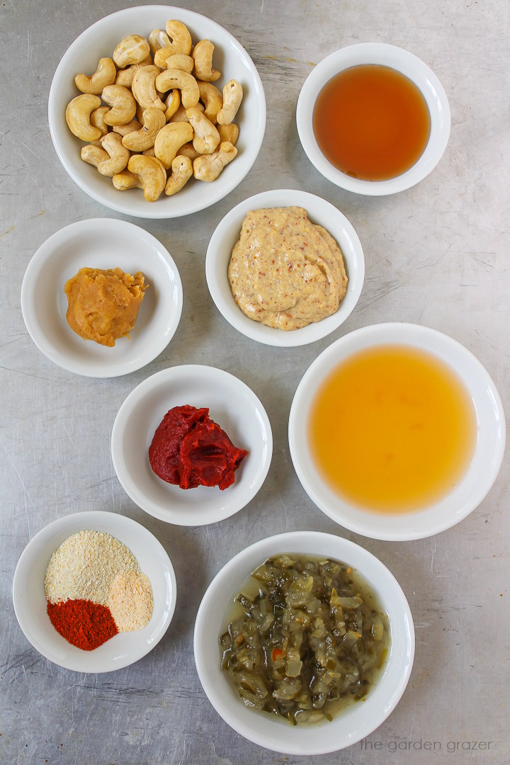 Raw cashews, vinegar, tomato paste, relish, mustard, and spice ingredients laid out on a metal tray