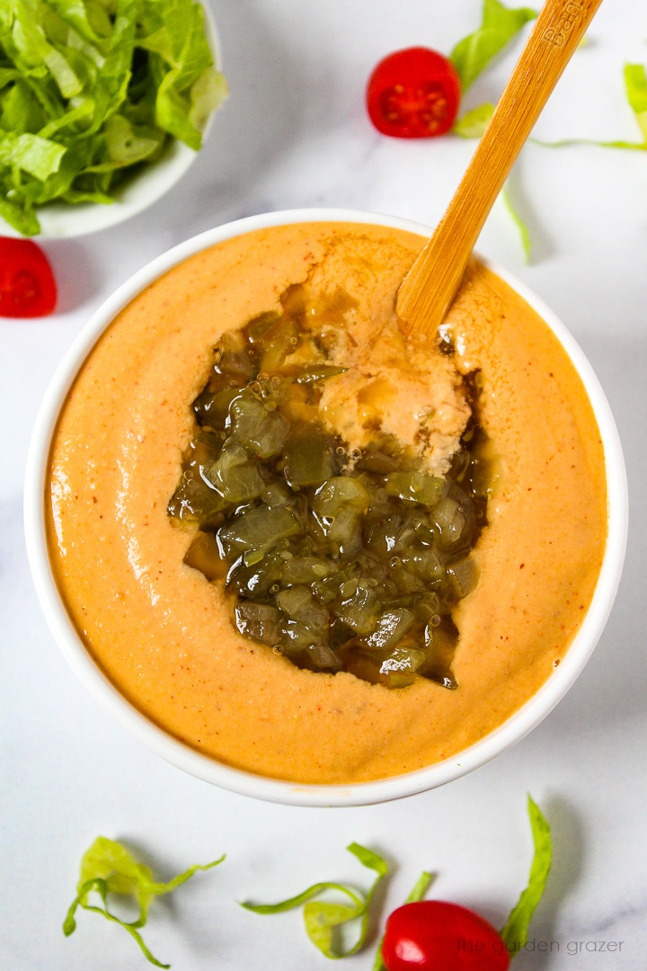 Overhead view of preparing vegan thousand island dressing in a small white bowl with stirring spoon