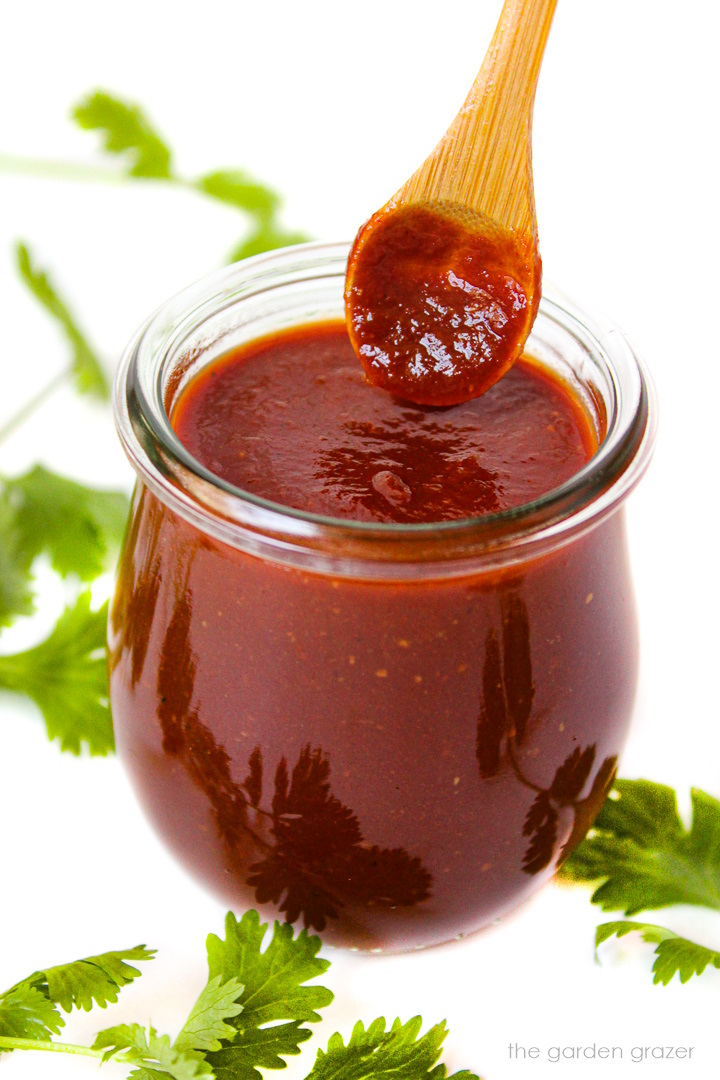 Vegan BBQ sauce in a small glass jar with wooden serving spoon