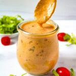 A spoon lifting up vegan thousand island dressing from a small glass serving jar