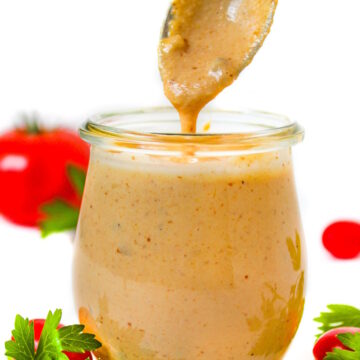 Spoon lifting up vegan thousand island dressing from a small glass jar