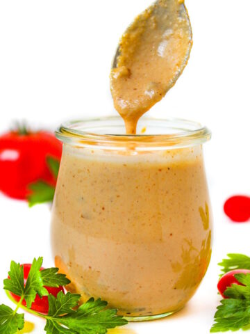 Spoon lifting up vegan thousand island dressing from a small glass jar