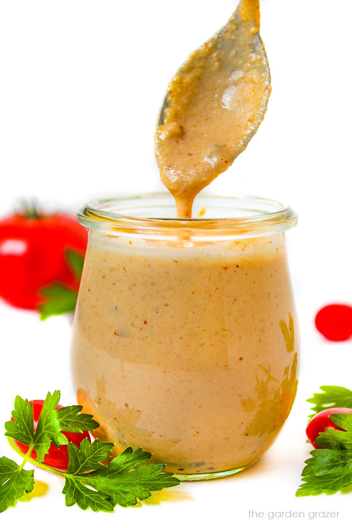 Spoon lifting up vegan thousand island dressing from a small glass jar