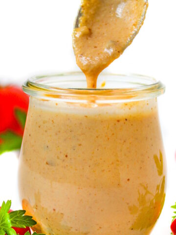 Spoon lifting up vegan thousand island dressing from a small glass jar