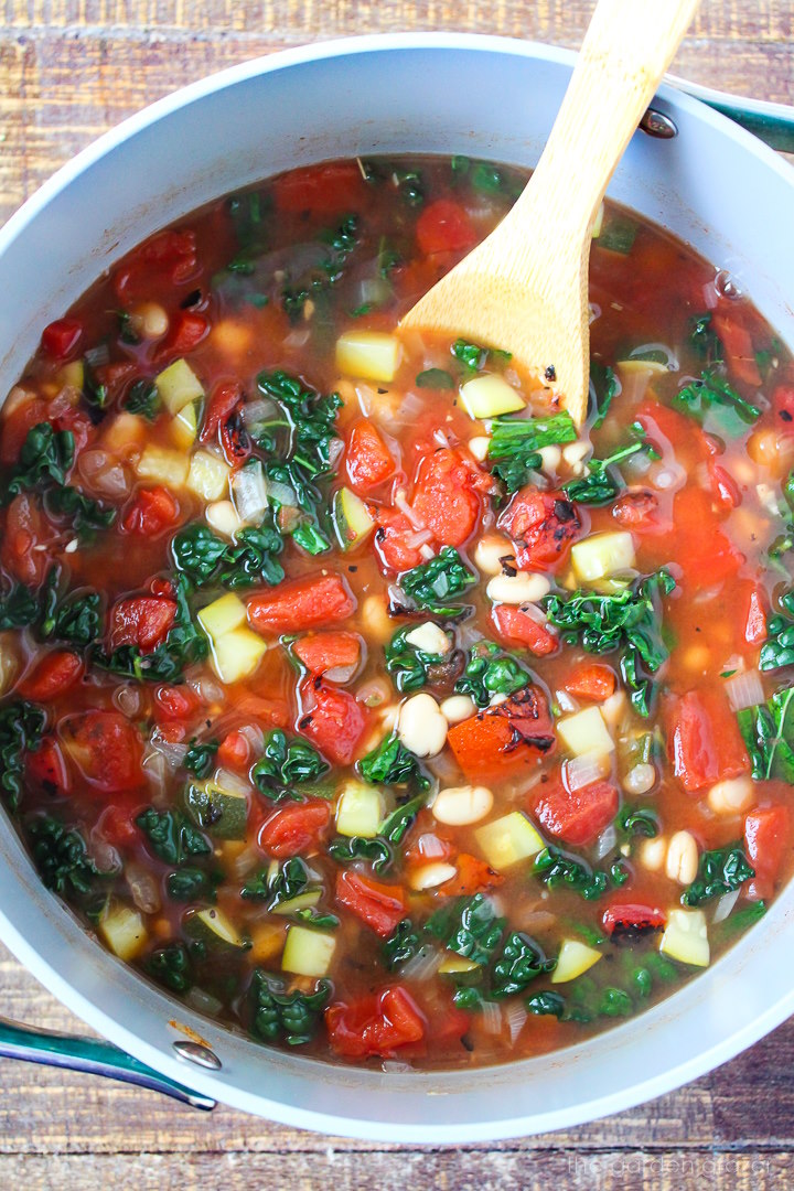 Overhead view of white bean tomato soup cooking in a large stockpot with wooden spoon
