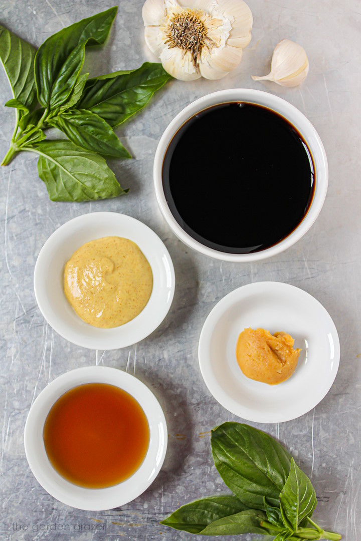 Vinegar, mustard, miso, maple syrup, and fresh herb ingredients laid out on a metal tray