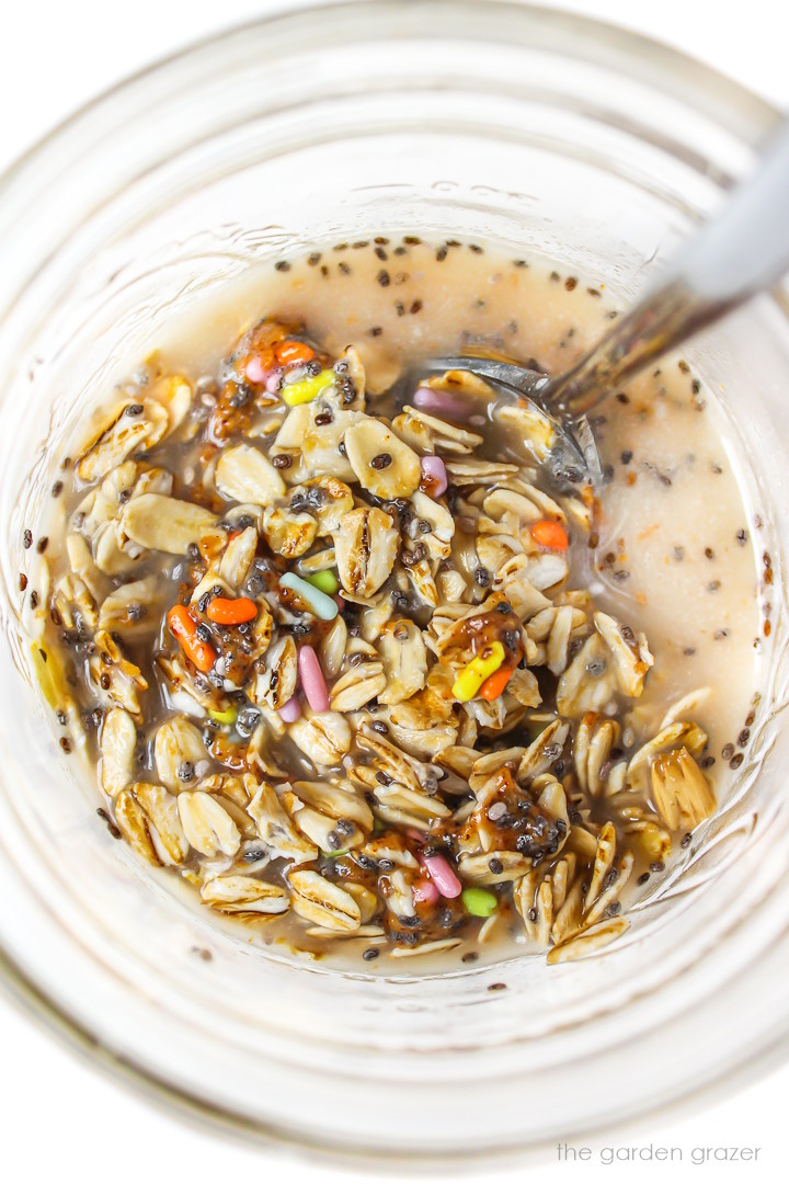 Overhead view of preparing oats in a small glass jar with stirring spoon