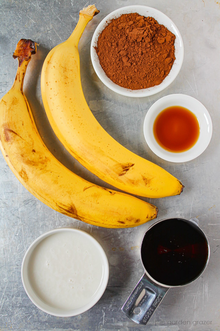 Cocoa powder, milk, maple syrup, and vanilla extract ingredients laid out on a metal tray