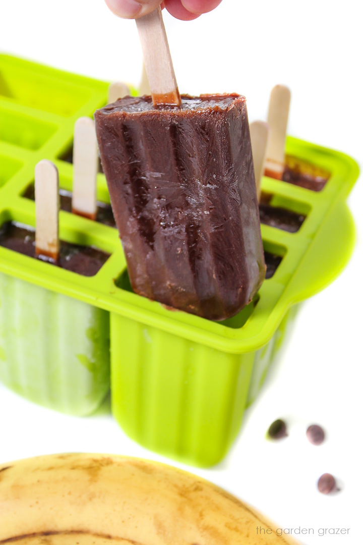 Chocolate banana popsicle being lifted out of a green popsicle mold