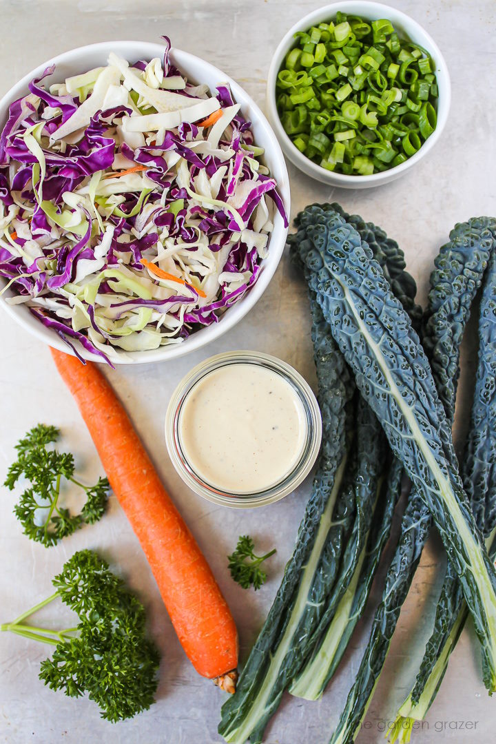 Dinosaur kale, carrot, shredded cabbage, parsley, and dressing ingredients laid out on a metal tray