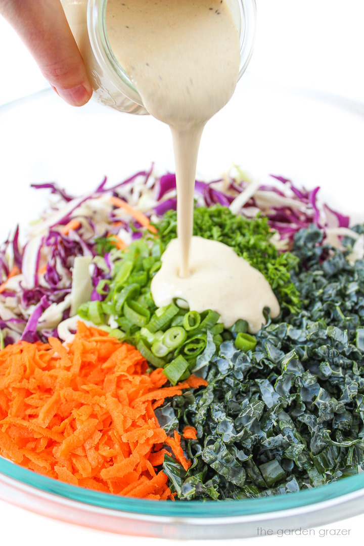 Creamy dressing being poured over salad ingredients in a large glass bowl