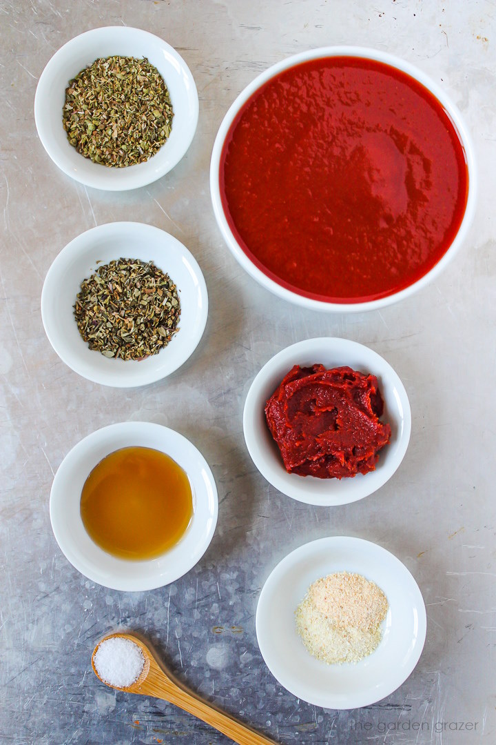 Tomato sauce, tomato paste, dried herbs, maple syrup, and spice ingredients laid out on a metal tray